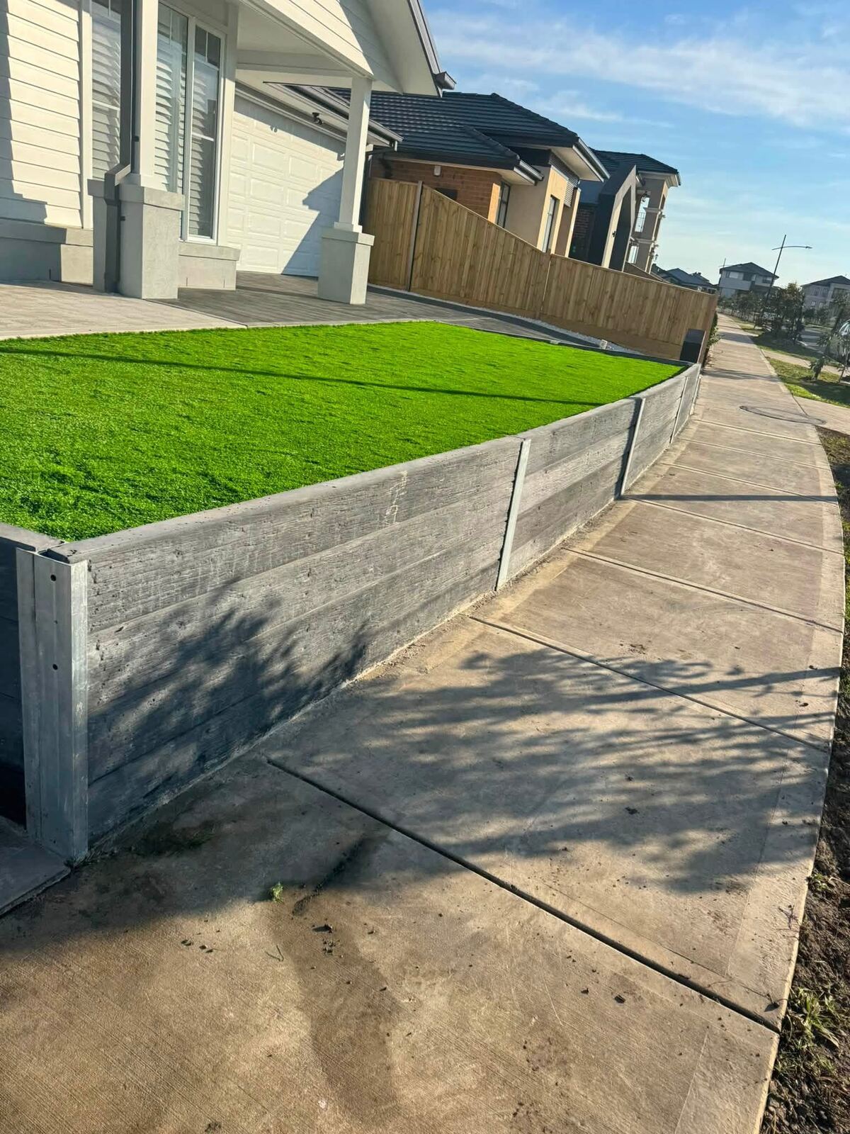 Sleeper retaining wall with artificial turf above a new concrete driveway edge