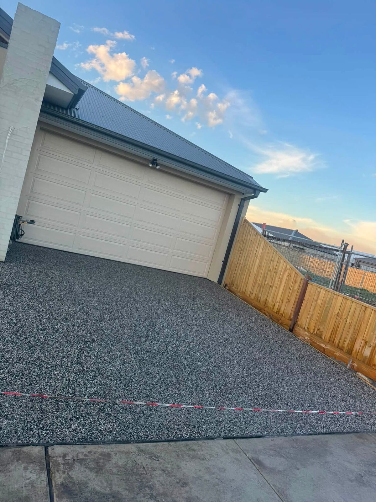 Exposed aggregate driveway freshly poured beside a timber fence