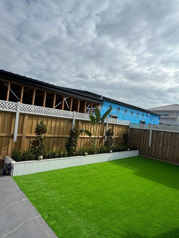 Artificial turf and garden bed with young plantings along a timber fence