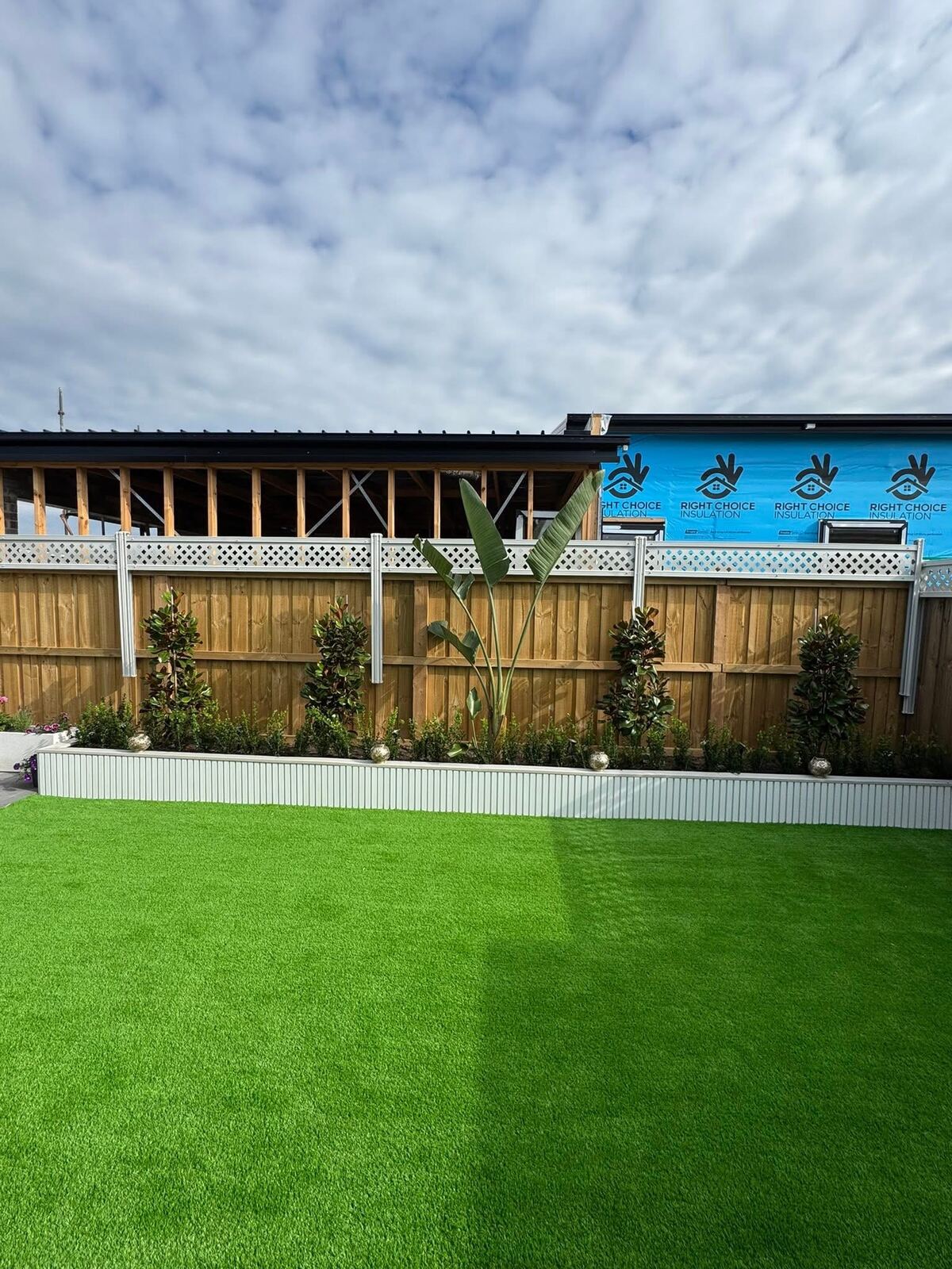 Artificial turf with garden bed and feature planting against a timber fence