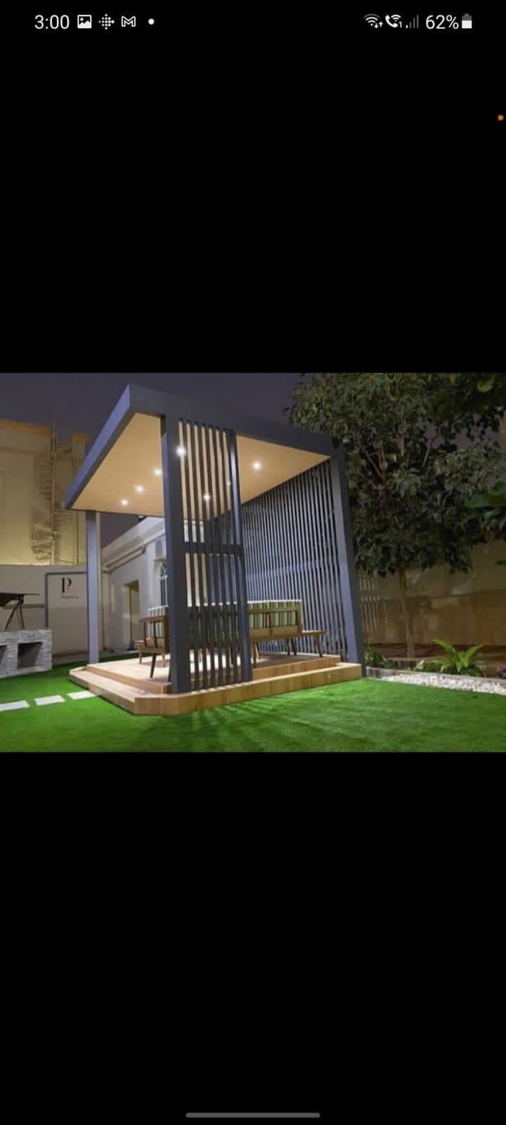 Lit outdoor room with pergola, bench seating and surrounding lawn at night